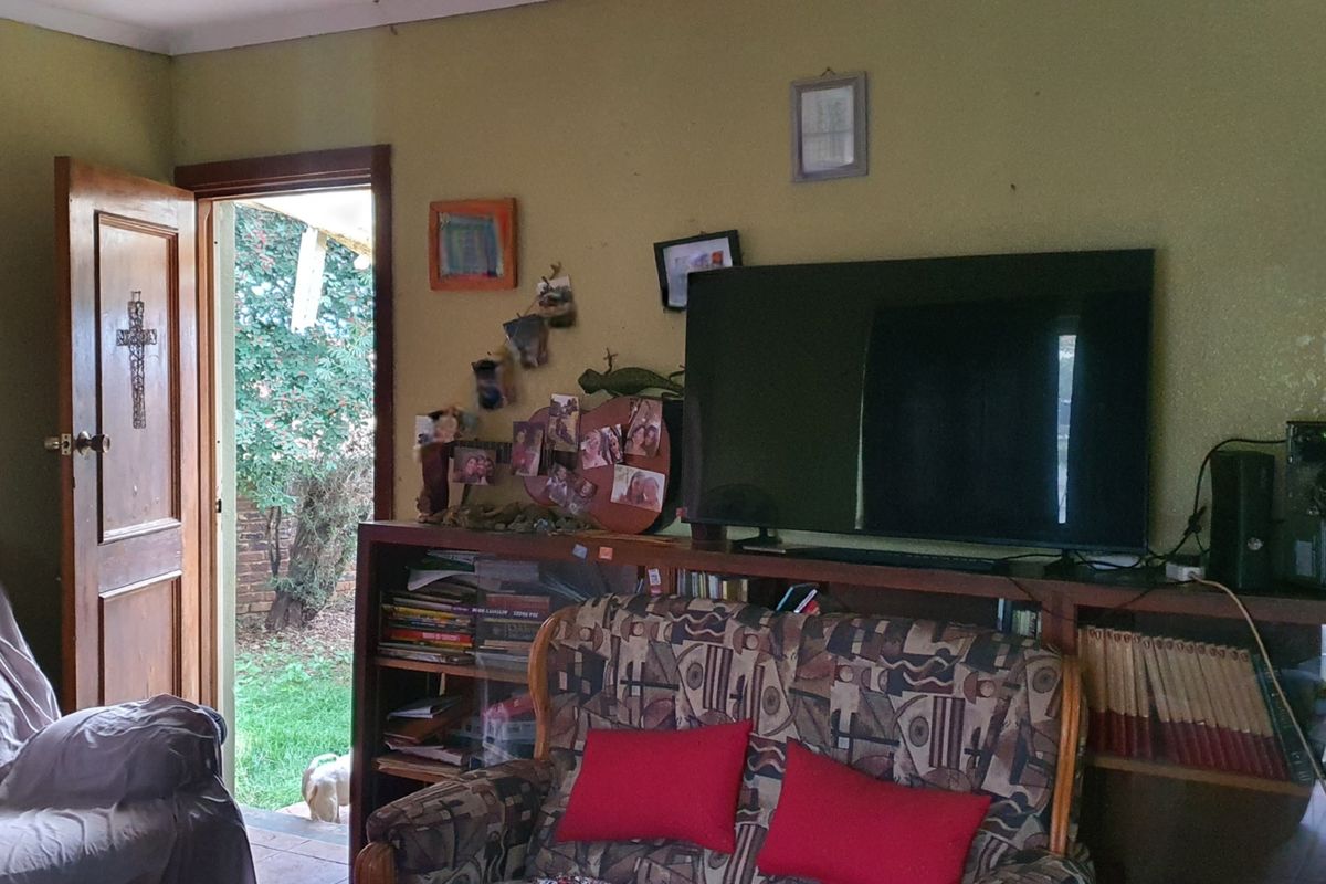 A living room area featuring a wooden door leading to the garden, with dated wall finishes and built-in shelving.