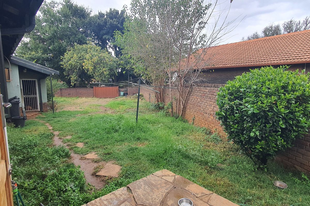 A rear garden area featuring a stone-paved patio, brick boundary walls, and an expansive lawn space with established trees.