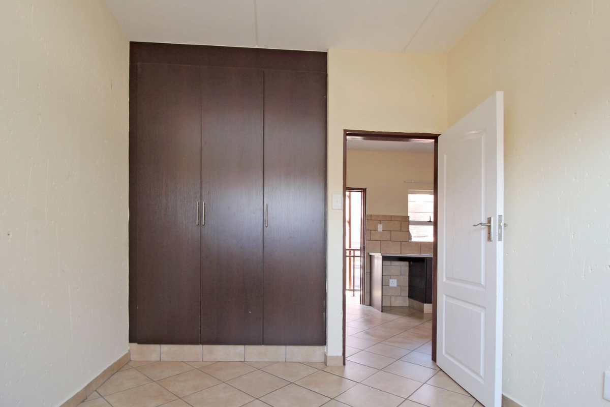 A bedroom featuring built-in dark wood cabinetry, tiled flooring, and a doorway leading to an adjacent kitchen area.