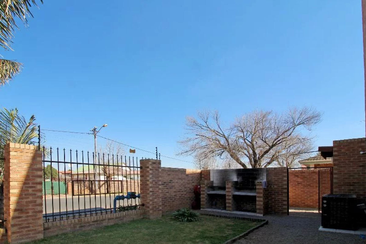 A private rear courtyard featuring a built-in brick braai area, enclosed by perimeter brick walls and metal security fencing.