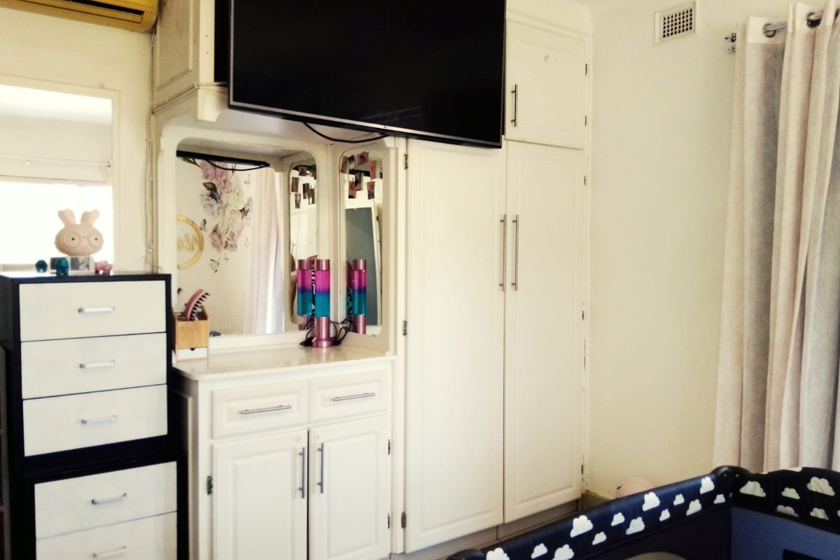 A bedroom featuring built-in white cabinetry with integrated vanity mirror and overhead storage, complemented by a wall-mounted air conditioning unit.