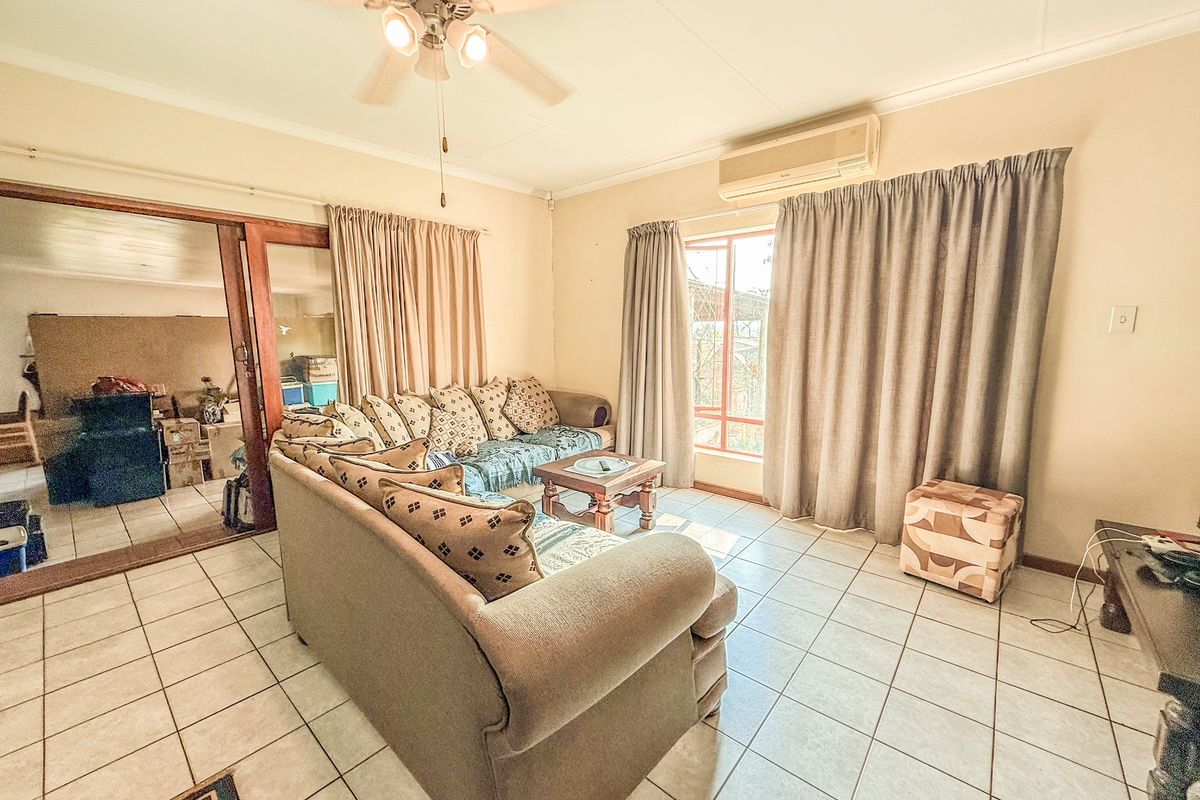 A living room featuring tiled flooring, a ceiling fan, and a wall-mounted air conditioning unit, with sliding glass doors leading to an adjacent room.