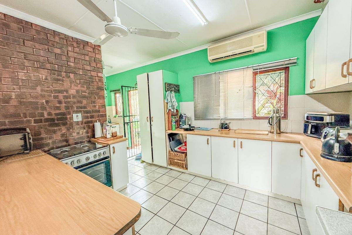 A functional kitchen featuring white cabinetry, wood-look countertops, a brick feature wall, and a ceiling fan, offering a practical layout for daily meal preparation.