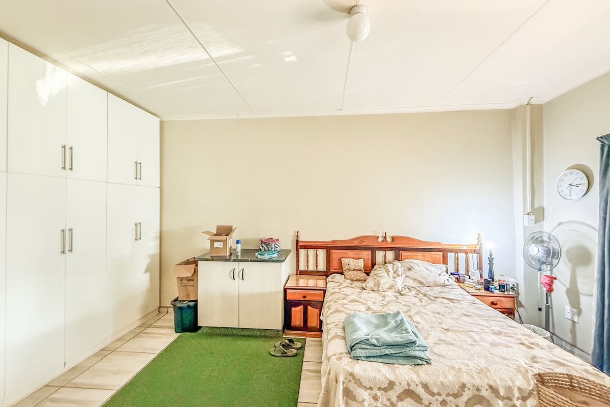 A functional bedroom featuring built-in white wardrobes, tiled flooring, and neutral wall tones, providing a practical and well-utilized living space.