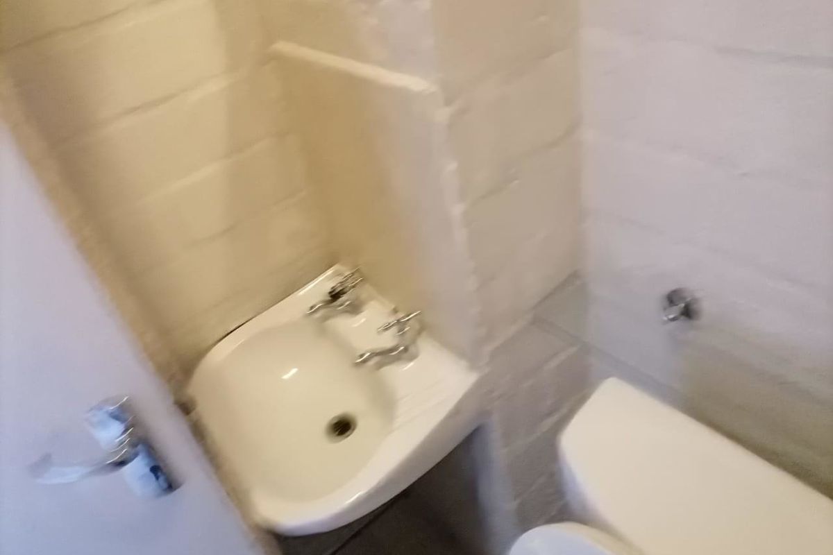 A compact bathroom featuring a wall-mounted basin and toilet with exposed painted brick walls.
