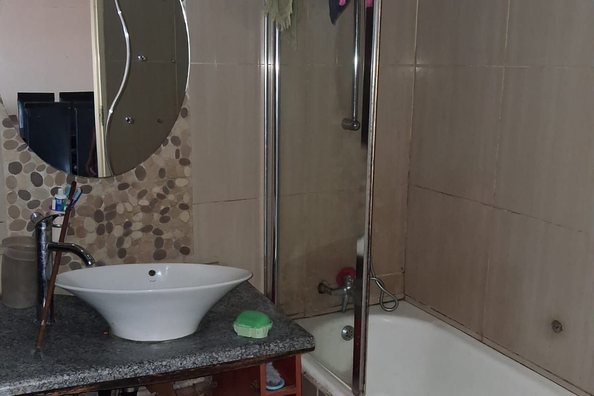 A bathroom featuring a vessel sink on a granite vanity, a bathtub with a glass screen, and decorative pebble-style wall tiling.