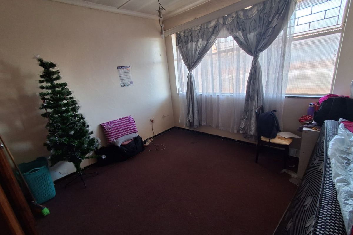 A bedroom featuring carpeted flooring, large windows with security bars, and basic wall finishes, offering a blank canvas for potential renovation.
