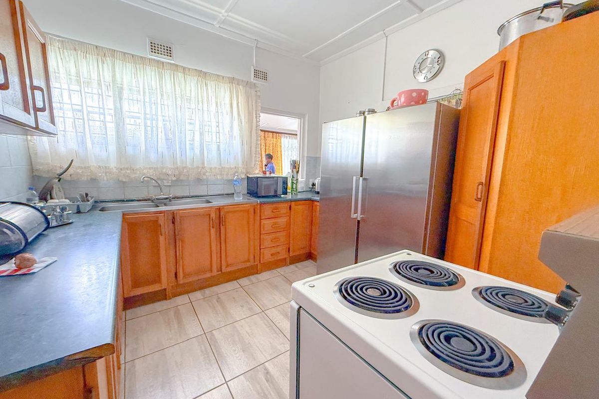 A functional kitchen featuring wooden cabinetry, tiled flooring, and a double basin sink with a view through to the adjacent living area.