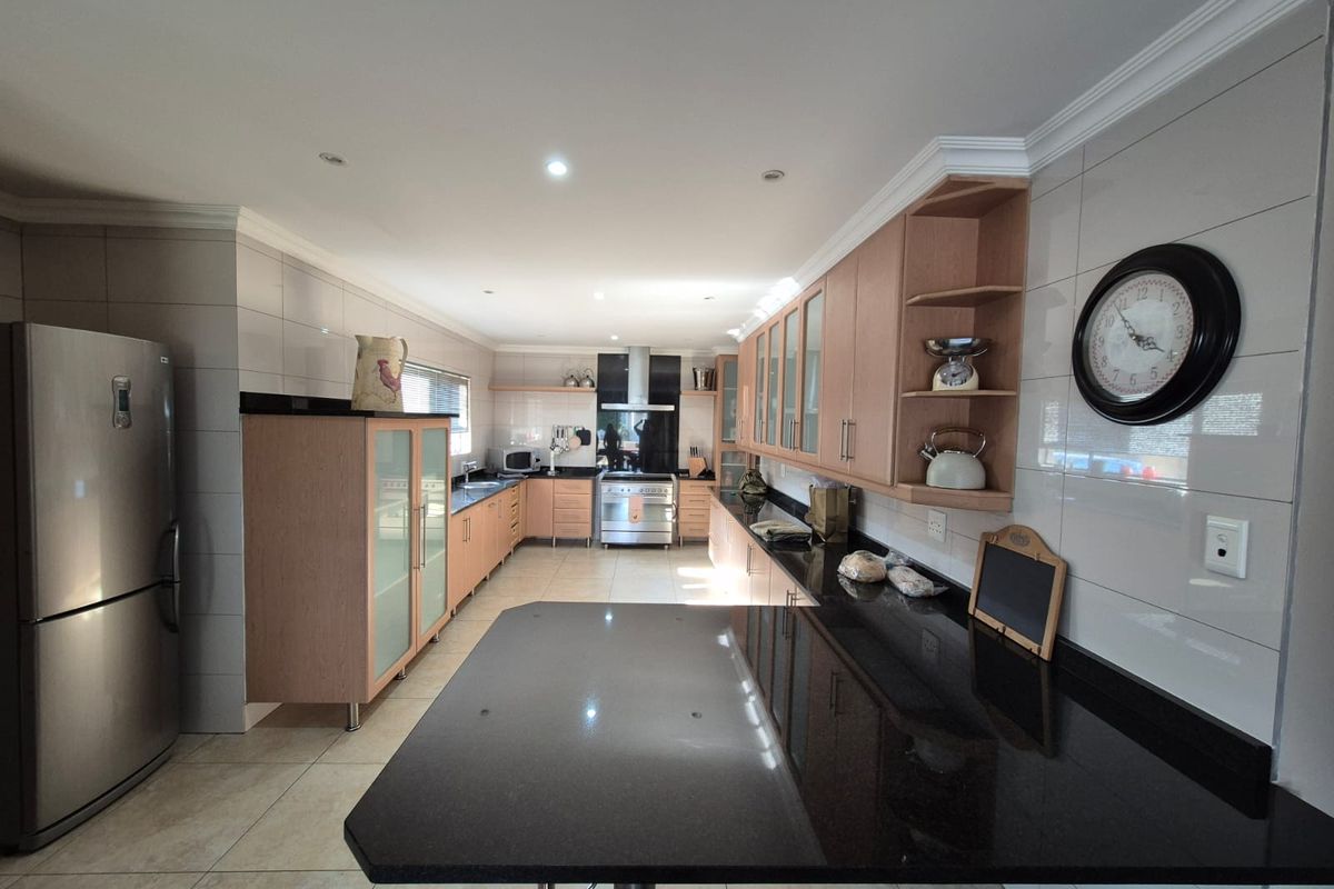 Spacious kitchen featuring light wood cabinetry, contrasting black granite countertops, a central breakfast bar, and integrated stainless steel appliances.