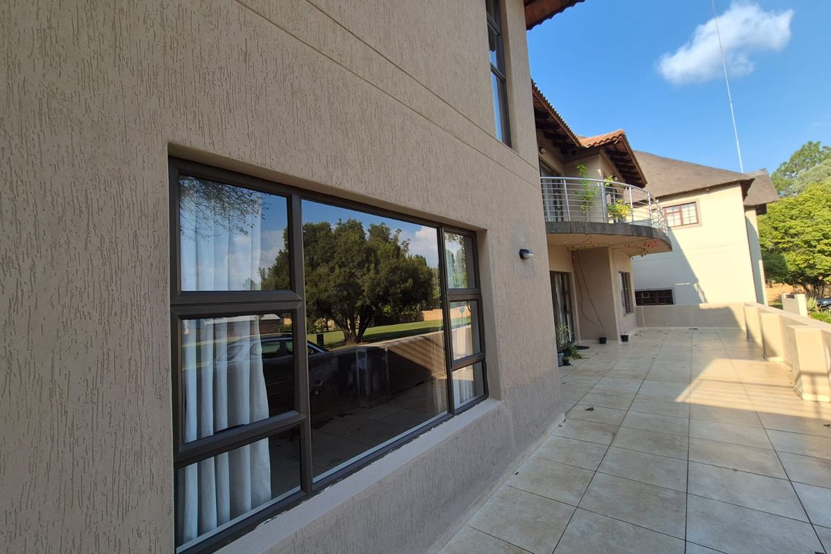 A view of the exterior rear facade featuring a tiled patio, large aluminum-framed windows, and an upper-level balcony with a metal railing.