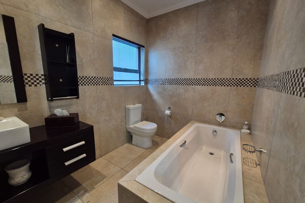 A well-maintained bathroom featuring a built-in bathtub, a modern vanity with a vessel sink, and a toilet, finished with neutral wall and floor tiles.