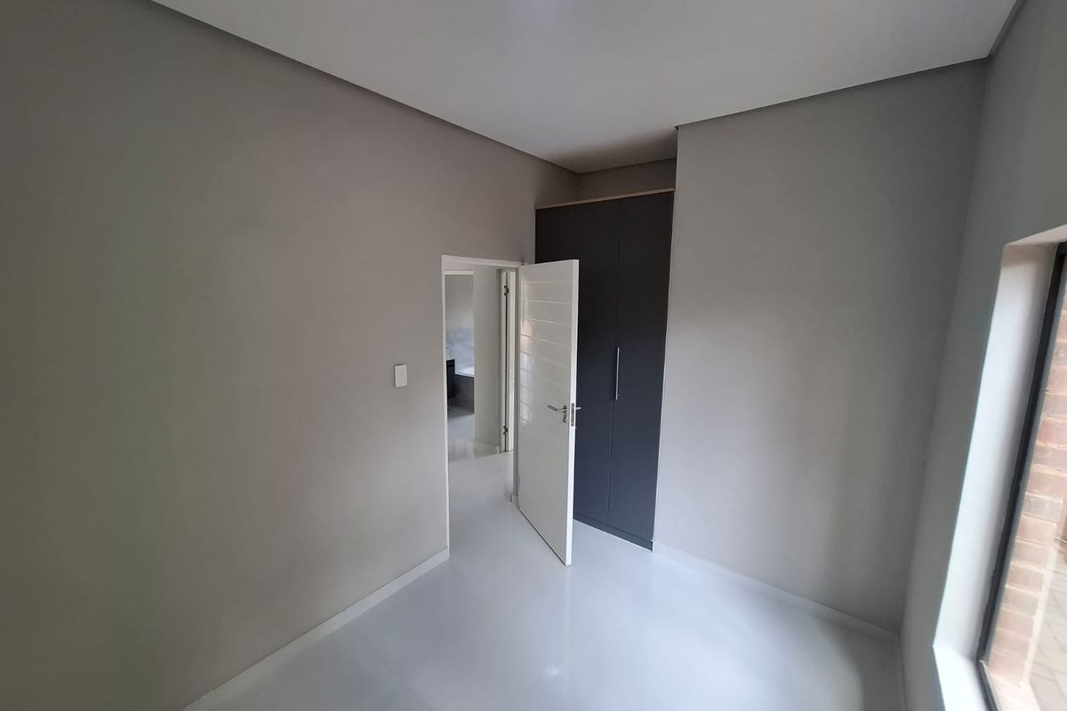 A clean, modern bedroom featuring neutral grey walls, white tiled flooring, and a built-in dark grey wardrobe.