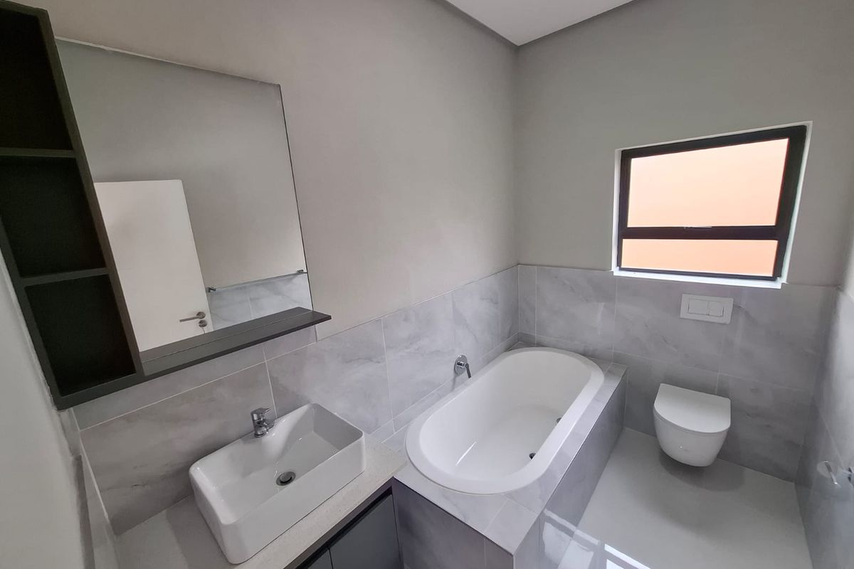 Modern bathroom featuring a sleek vanity with vessel sink, built-in bathtub, wall-mounted toilet, and contemporary grey marble-look tiling.