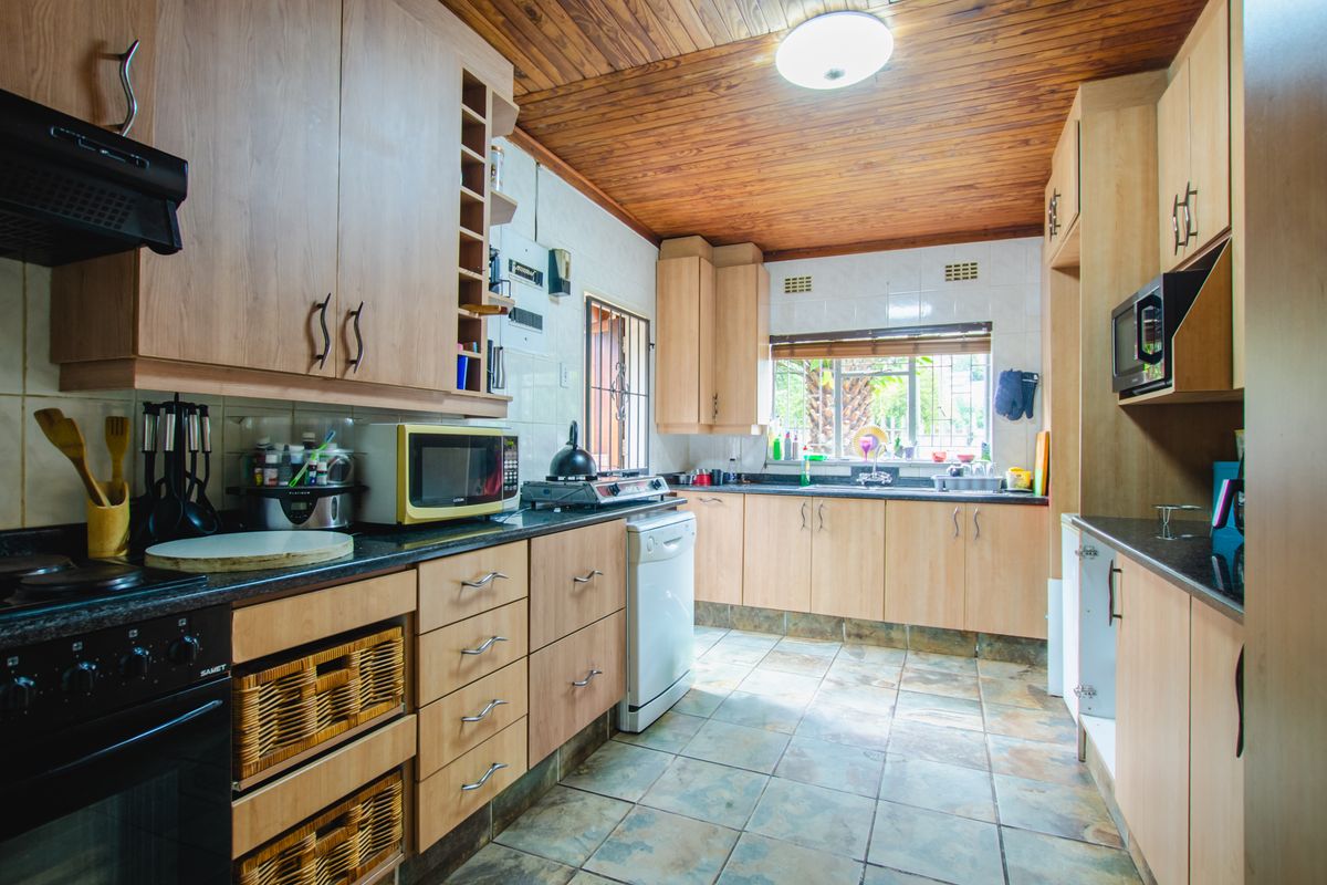 A functional kitchen featuring light wood-finish cabinetry, dark granite countertops, tiled flooring, and a timber-paneled ceiling with integrated storage solutions.