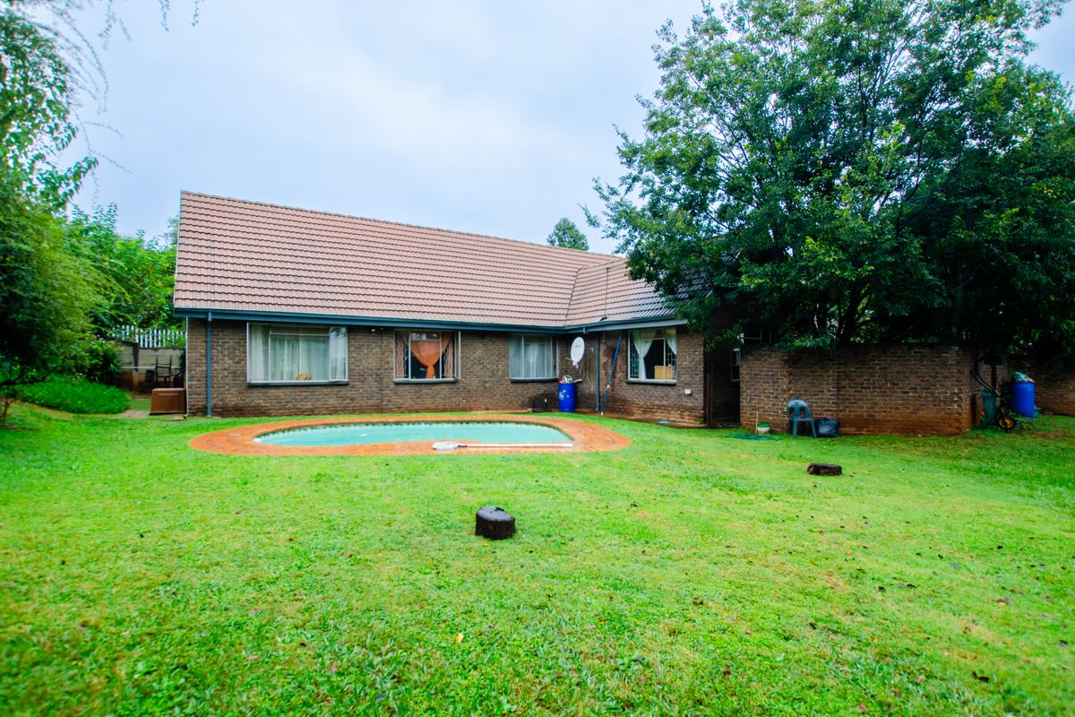 Rear view of a brick house featuring a swimming pool set within a spacious garden area.