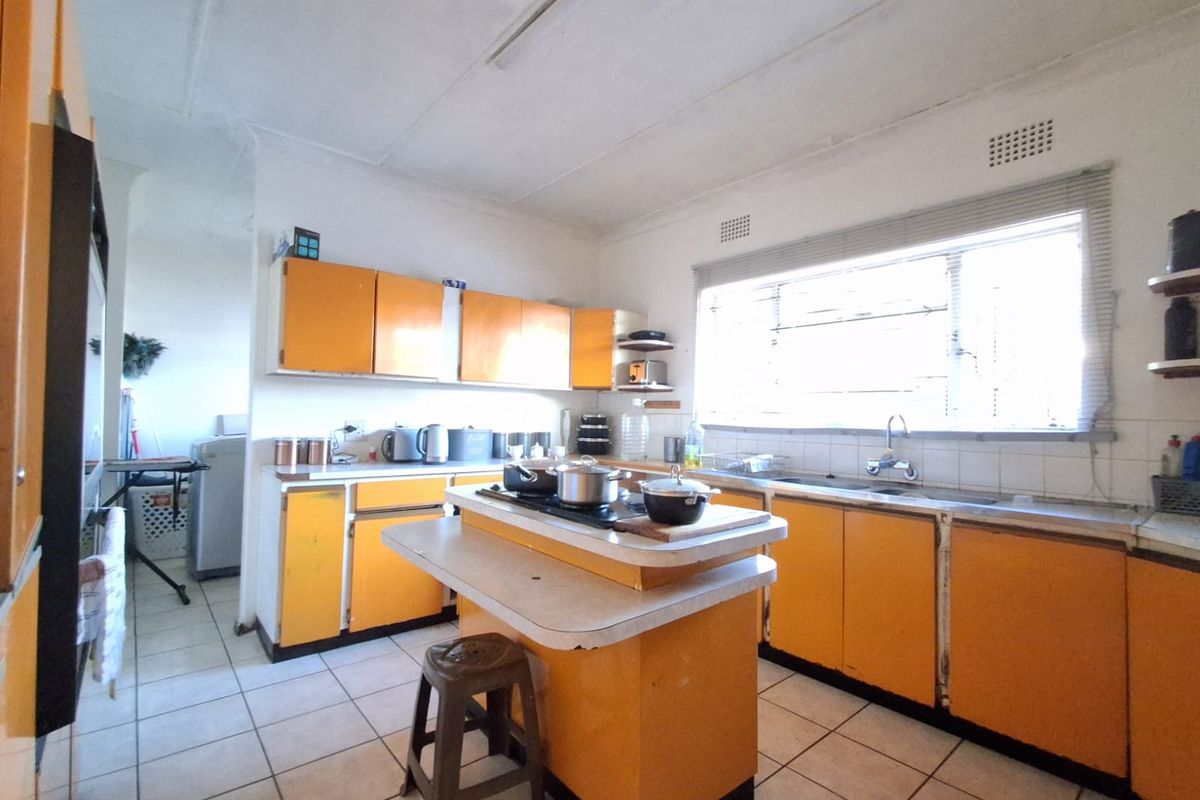 A dated kitchen featuring original orange cabinetry, a central island with a built-in cooktop, tiled flooring, and a large window providing natural light.