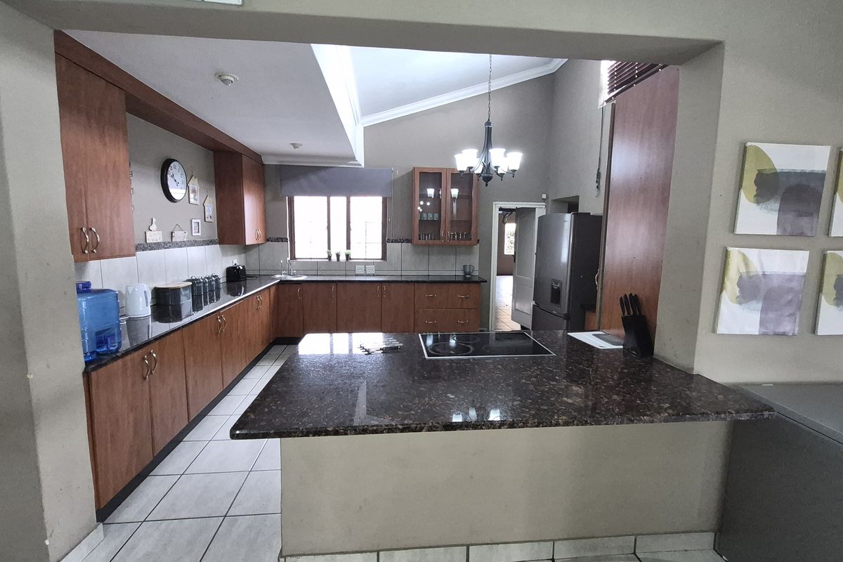Spacious kitchen featuring dark granite countertops, wooden cabinetry, a central island with a built-in hob, and tiled flooring.