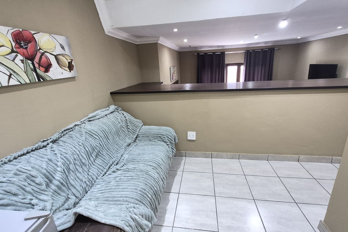 A living area featuring tiled flooring, recessed ceiling lighting, and a half-wall partition overlooking an adjacent space.