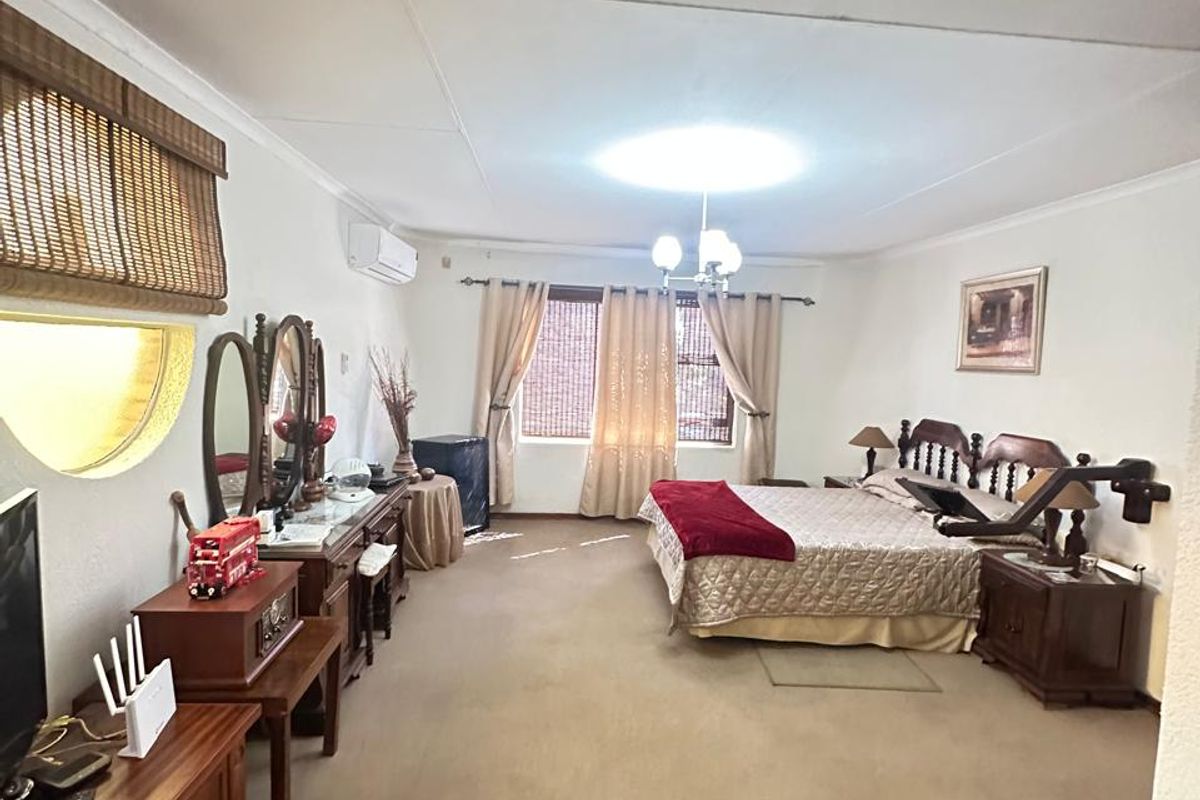 Spacious bedroom featuring neutral walls, carpeted flooring, a wall-mounted air conditioning unit, and a unique circular window with bamboo blinds.