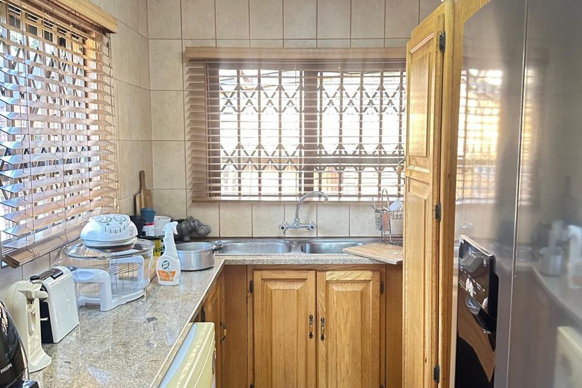 A functional kitchen featuring granite countertops, wooden cabinetry, double stainless steel sink, and tiled walls and flooring.