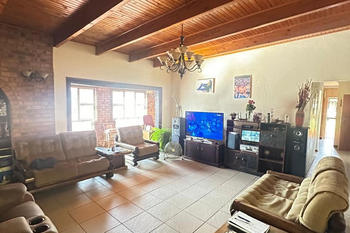 Spacious living room featuring a high vaulted timber-beamed ceiling, exposed brick fireplace, and large windows providing ample natural light.