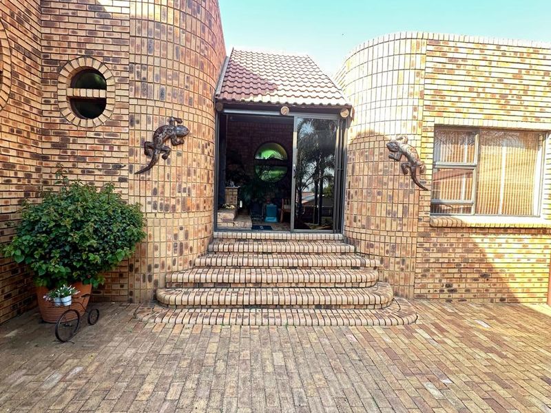 A unique face-brick exterior entrance featuring curved walls, a tiled roof section, and a paved courtyard leading to a sliding glass door.
