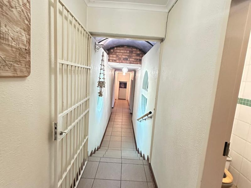 A narrow interior hallway featuring tiled flooring, a security gate, and a vaulted brick ceiling section leading to further living areas.