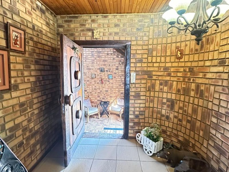 An entrance foyer featuring exposed face-brick walls, a timber-clad ceiling, and tiled flooring, leading through a solid timber door to an outdoor patio area.