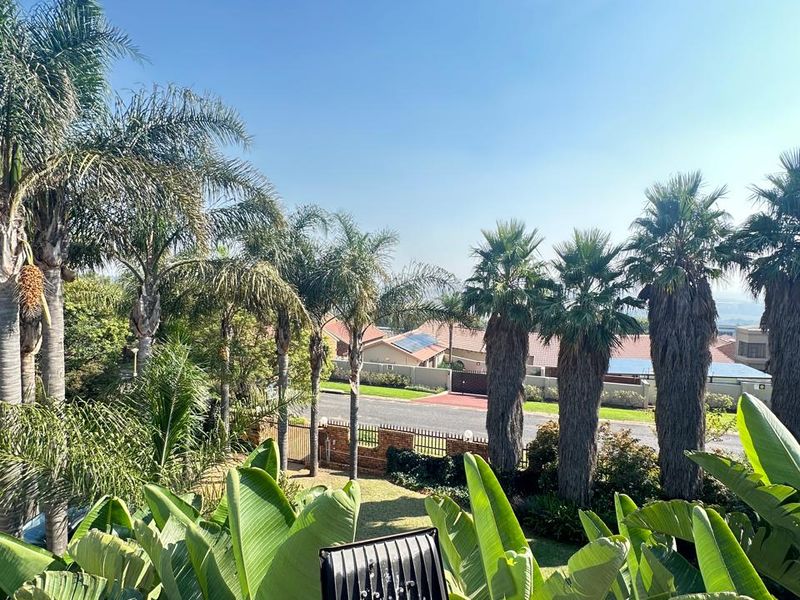 Elevated view from a balcony overlooking a landscaped garden, palm trees, and the surrounding residential street.