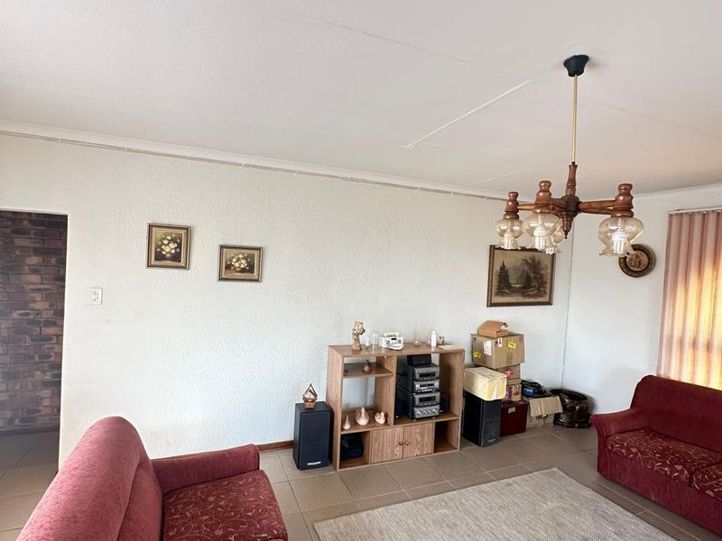 A spacious living room featuring tiled flooring, a traditional chandelier, and textured wall finishes, offering a functional layout for comfortable family living.