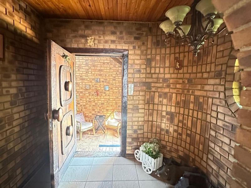 Entrance foyer featuring exposed face-brick walls, tiled flooring, and a timber-clad ceiling, leading through an arched doorway to an outdoor patio area.