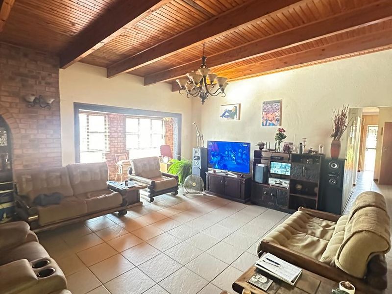 Spacious living room featuring a high vaulted timber-beamed ceiling, exposed brick fireplace, and large windows providing ample natural light.