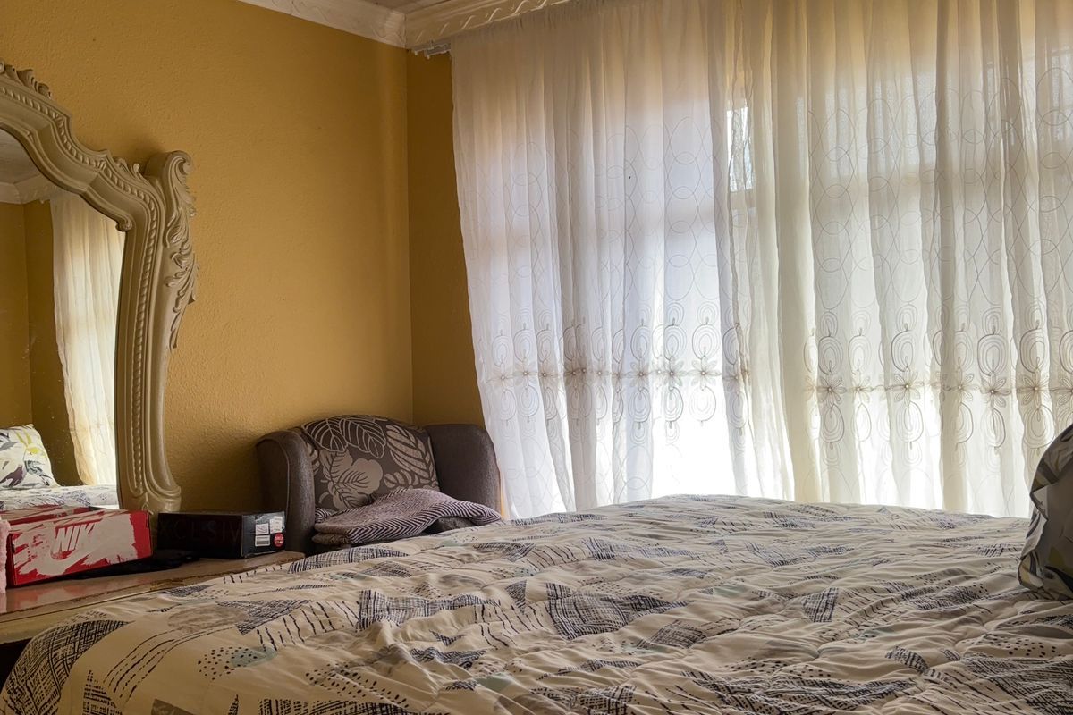 A bedroom featuring textured ceiling finishes, yellow wall paint, and large windows with sheer curtains.