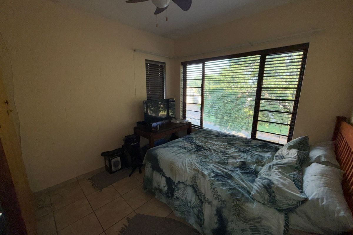 A bedroom featuring tiled flooring, a ceiling fan, and large windows with fitted blinds, providing natural light and views of the surrounding area.