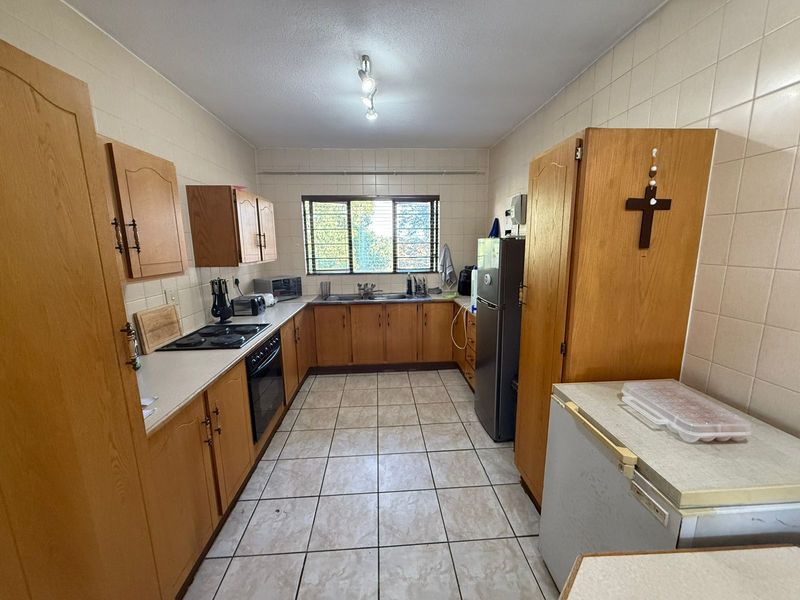 A functional kitchen featuring wooden cabinetry, tiled flooring, a built-in oven and hob, and a window providing natural light.