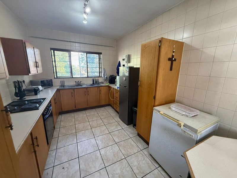 A functional kitchen featuring wooden cabinetry, tiled walls, a built-in hob and oven, and a stainless steel sink under a window.