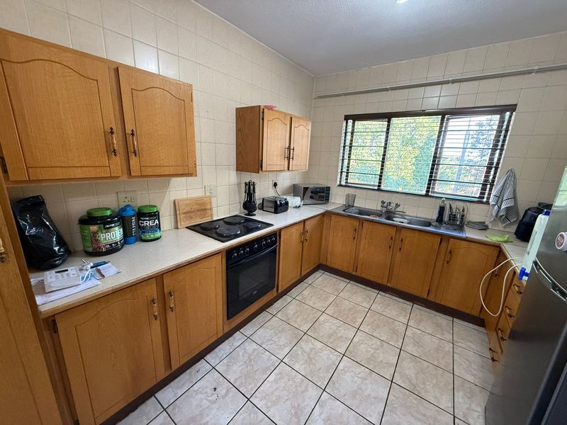 A functional kitchen featuring wooden cabinetry, tiled splashbacks, a built-in oven and hob, and a double sink with a window view.