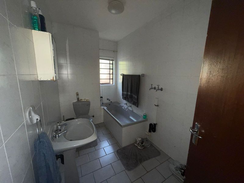 A functional bathroom featuring a pedestal basin, a built-in bathtub, and tiled walls and flooring, offering a blank canvas for potential renovation.
