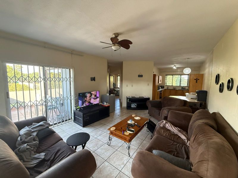 Open-plan living and kitchen area featuring tiled flooring, a ceiling fan, and sliding glass doors with security gates leading to an outdoor patio.