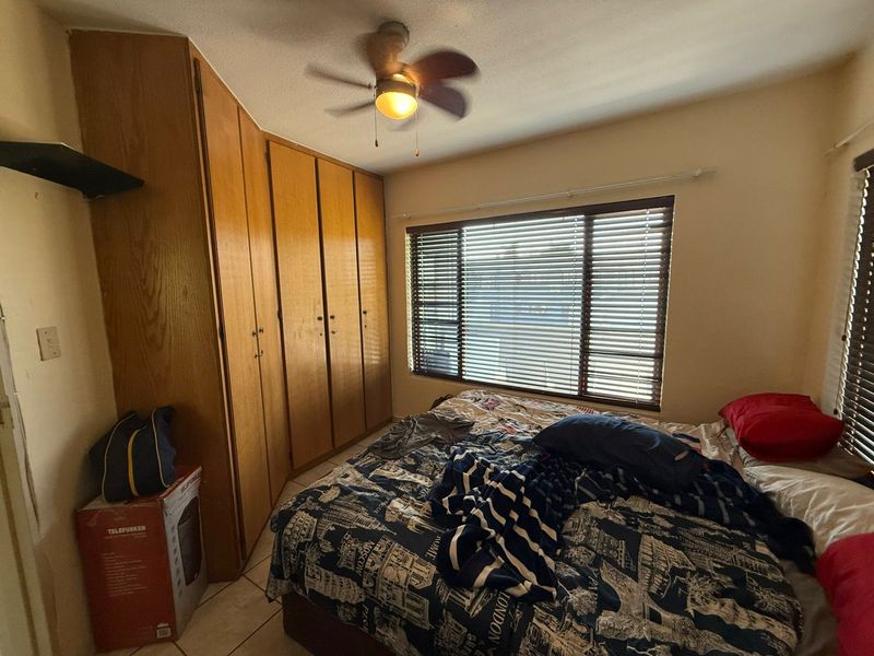 A bedroom featuring built-in wooden cabinetry, a ceiling fan, and large windows with fitted blinds.