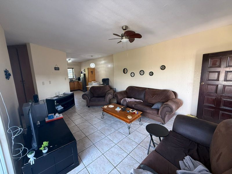 Open plan living area featuring tiled flooring, a ceiling fan, and an adjoining kitchen space with built-in cabinetry.