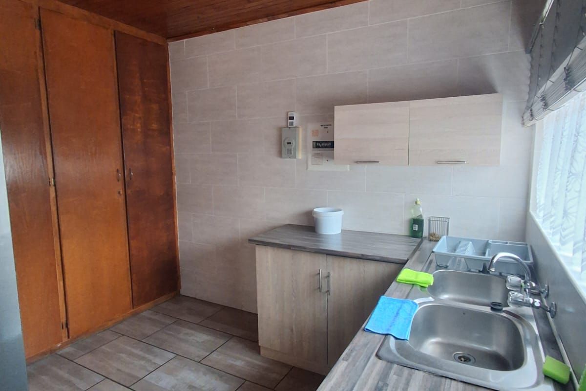 A functional kitchen area featuring tiled flooring, wood-paneled ceiling, built-in cabinetry, and a stainless steel double sink with laminate countertops.