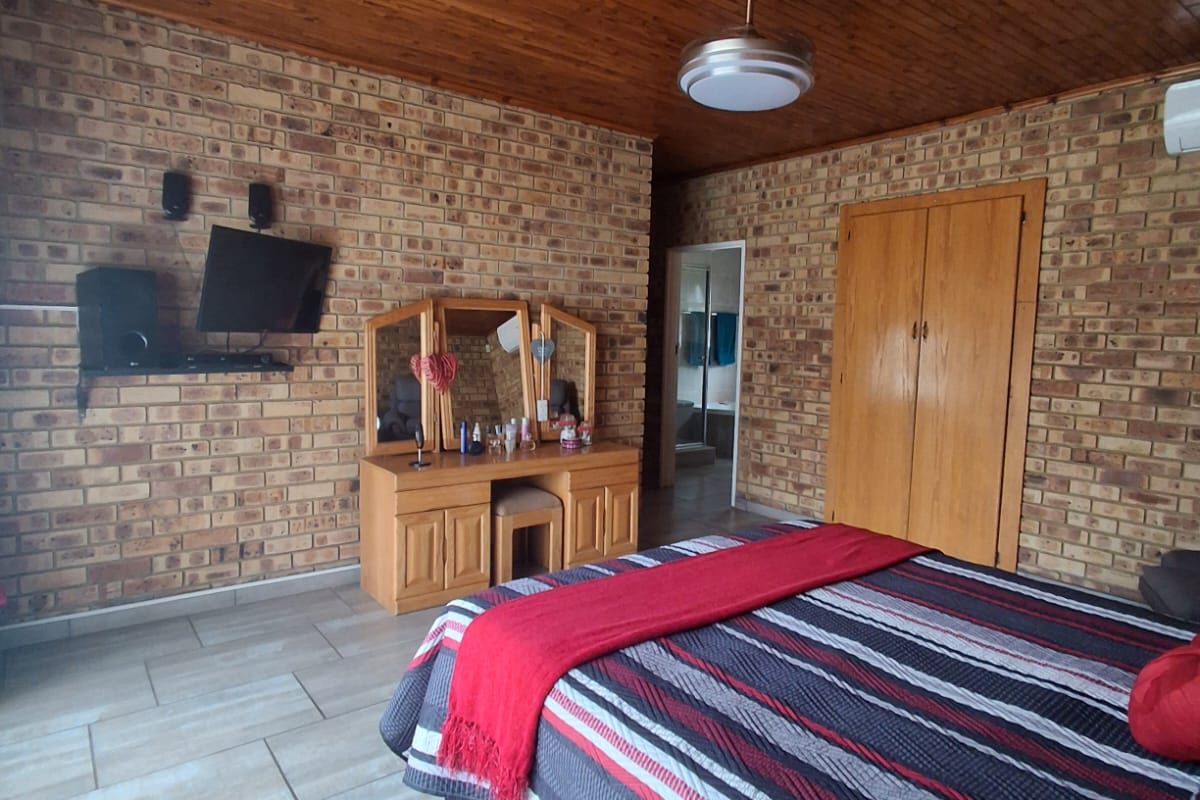 A bedroom featuring exposed brick walls, a timber-paneled ceiling, tiled flooring, and built-in wooden cupboards.