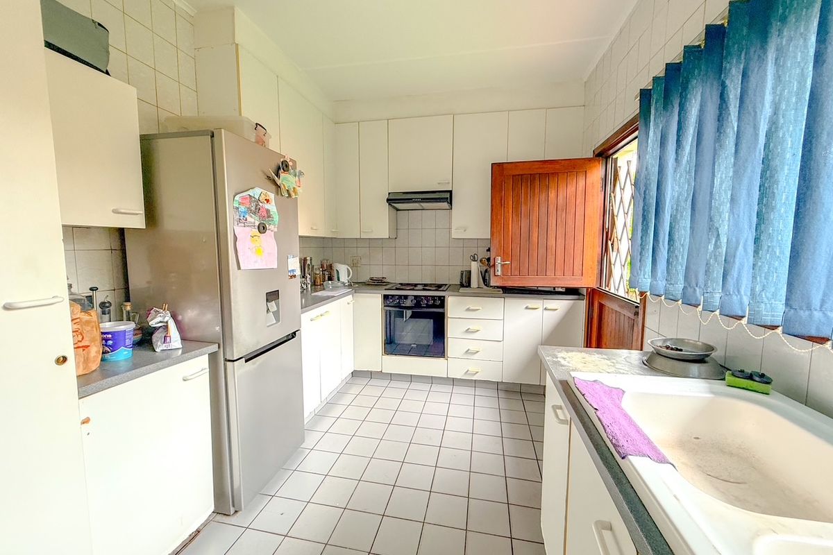 Functional kitchen featuring white cabinetry, tiled flooring, built-in oven, hob, extractor fan, and a double basin sink with direct exterior access.