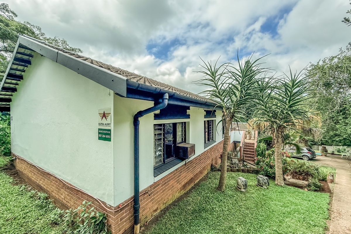 Side view of the house featuring a brick and plaster facade, tiled roof, guttering system, and window-mounted air conditioning unit.