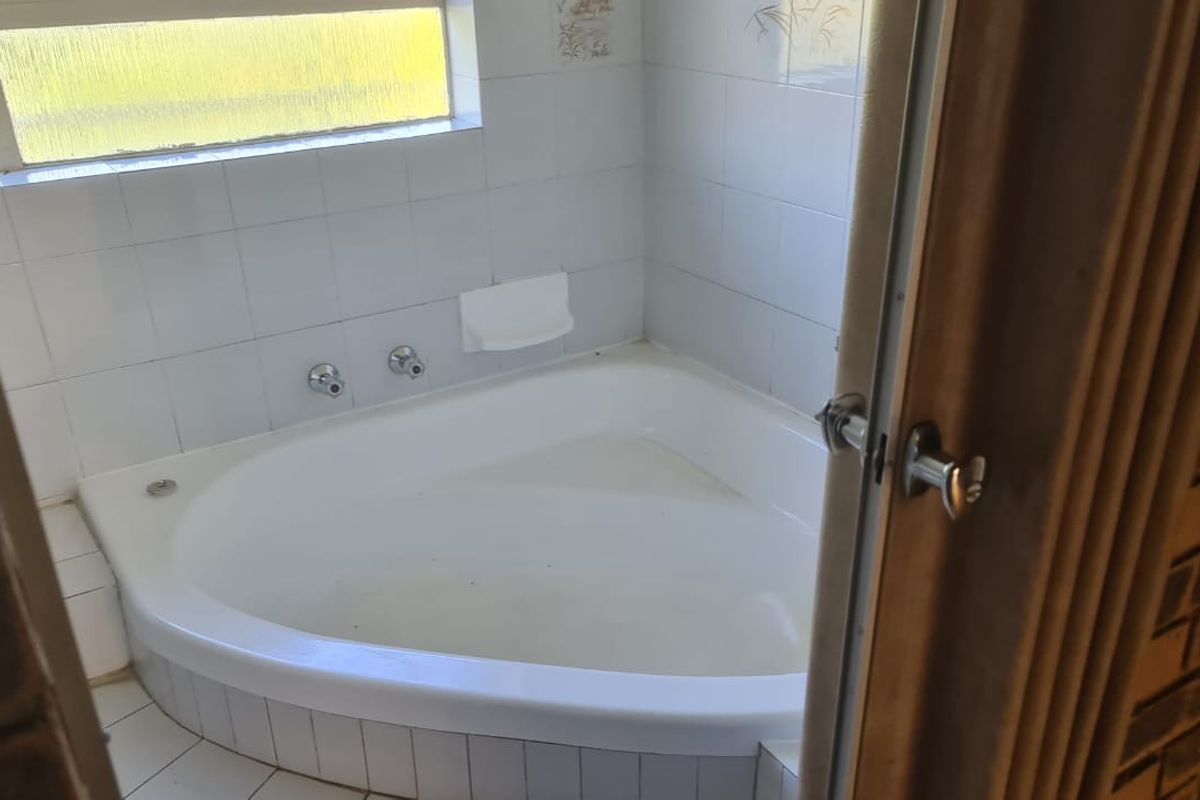 A functional bathroom featuring a corner bathtub with white wall tiling and a window for natural light.