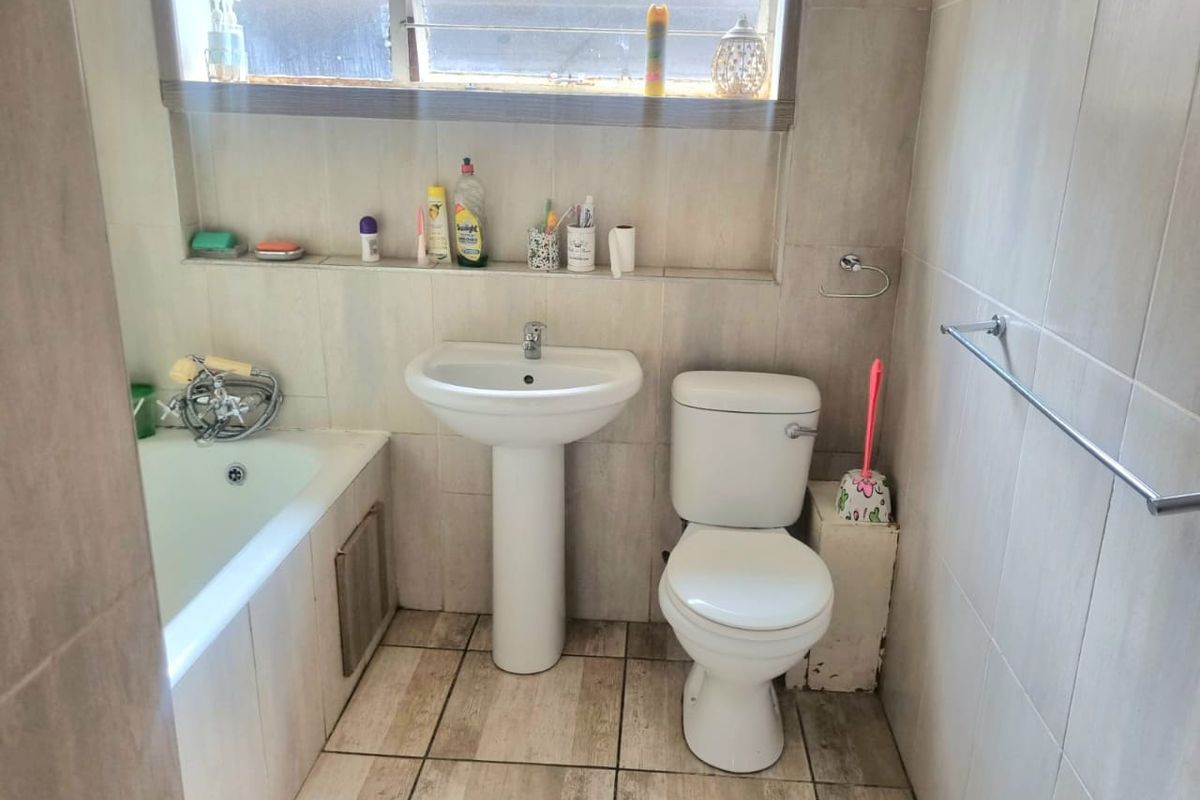 A functional bathroom featuring a pedestal basin, toilet, and bathtub with tiled walls and flooring.