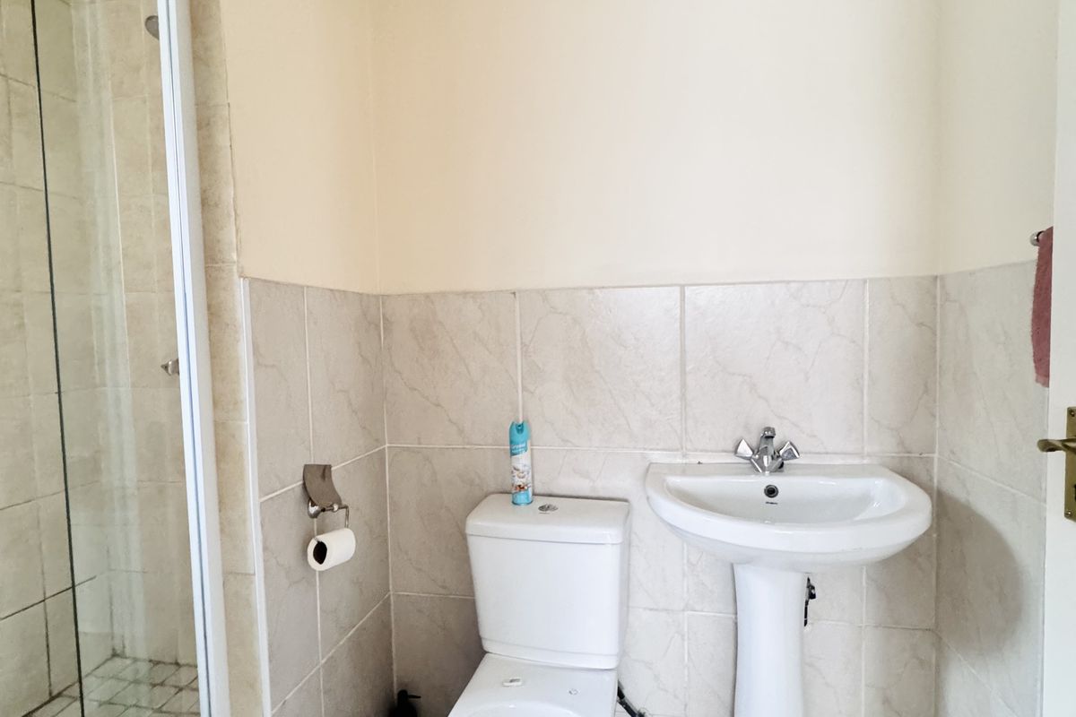 A functional bathroom featuring a pedestal sink, a standard toilet, and a glass-enclosed shower with tiled walls and flooring.