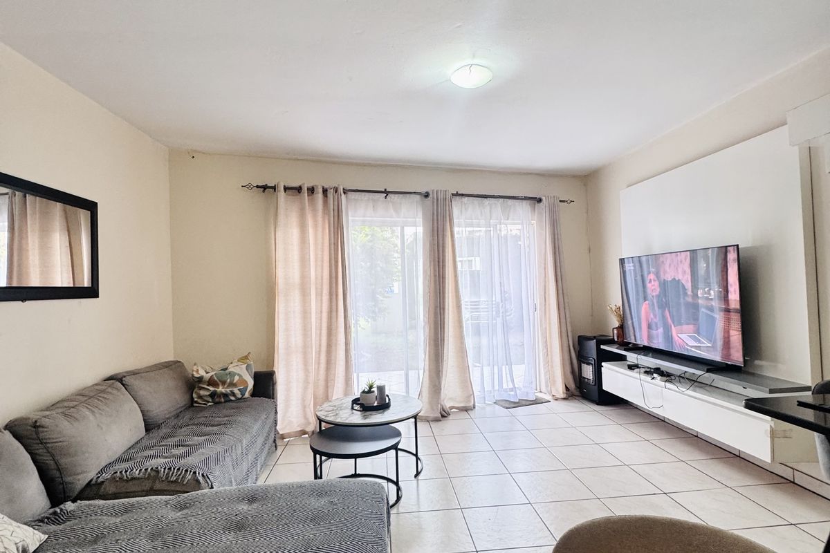 A bright living room featuring large sliding glass doors, neutral floor tiles, and a built-in media console unit.