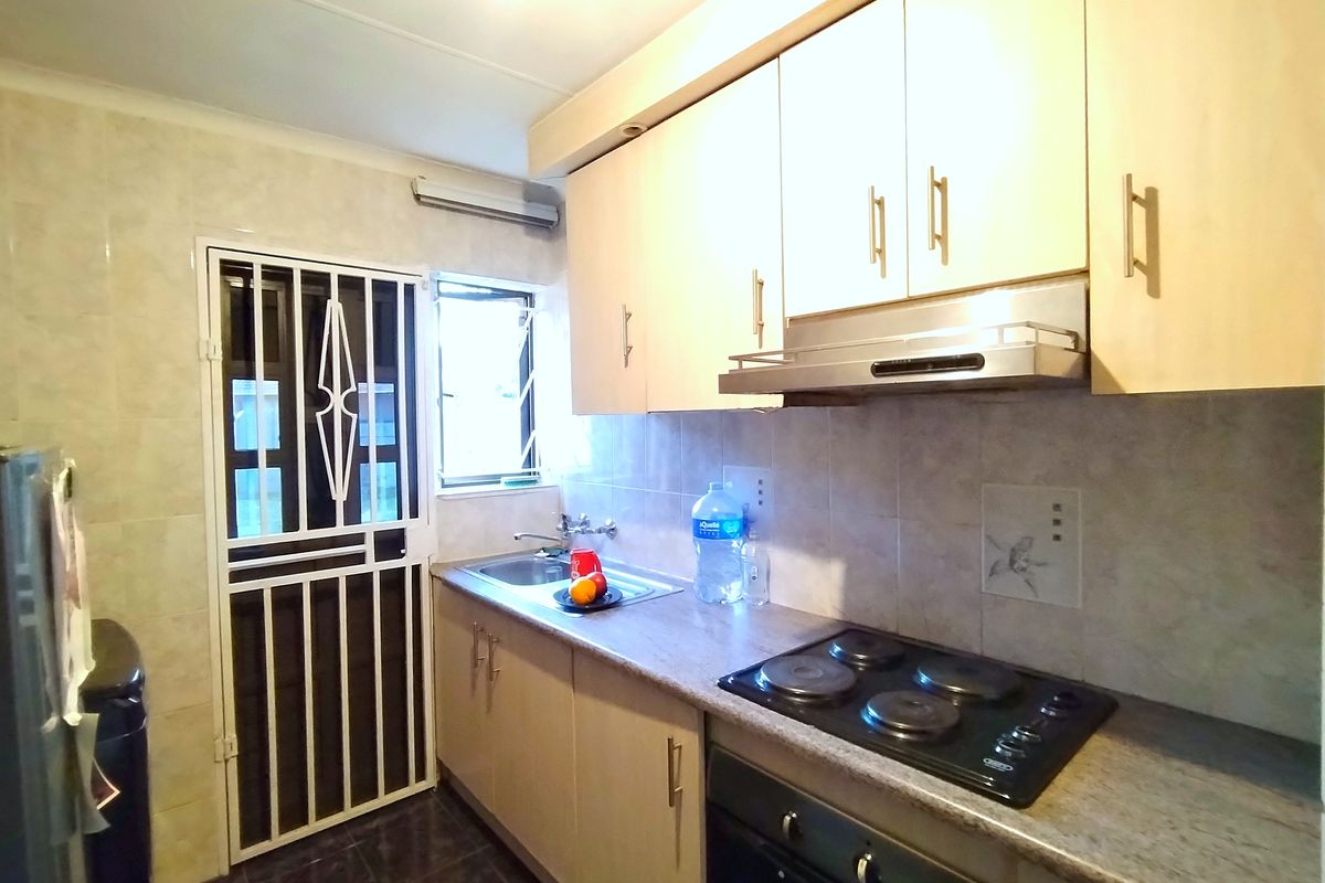 Functional kitchen featuring light-toned cabinetry, laminate countertops, integrated electric hob, oven, extractor fan, and tiled splashback with a secure exterior access door.